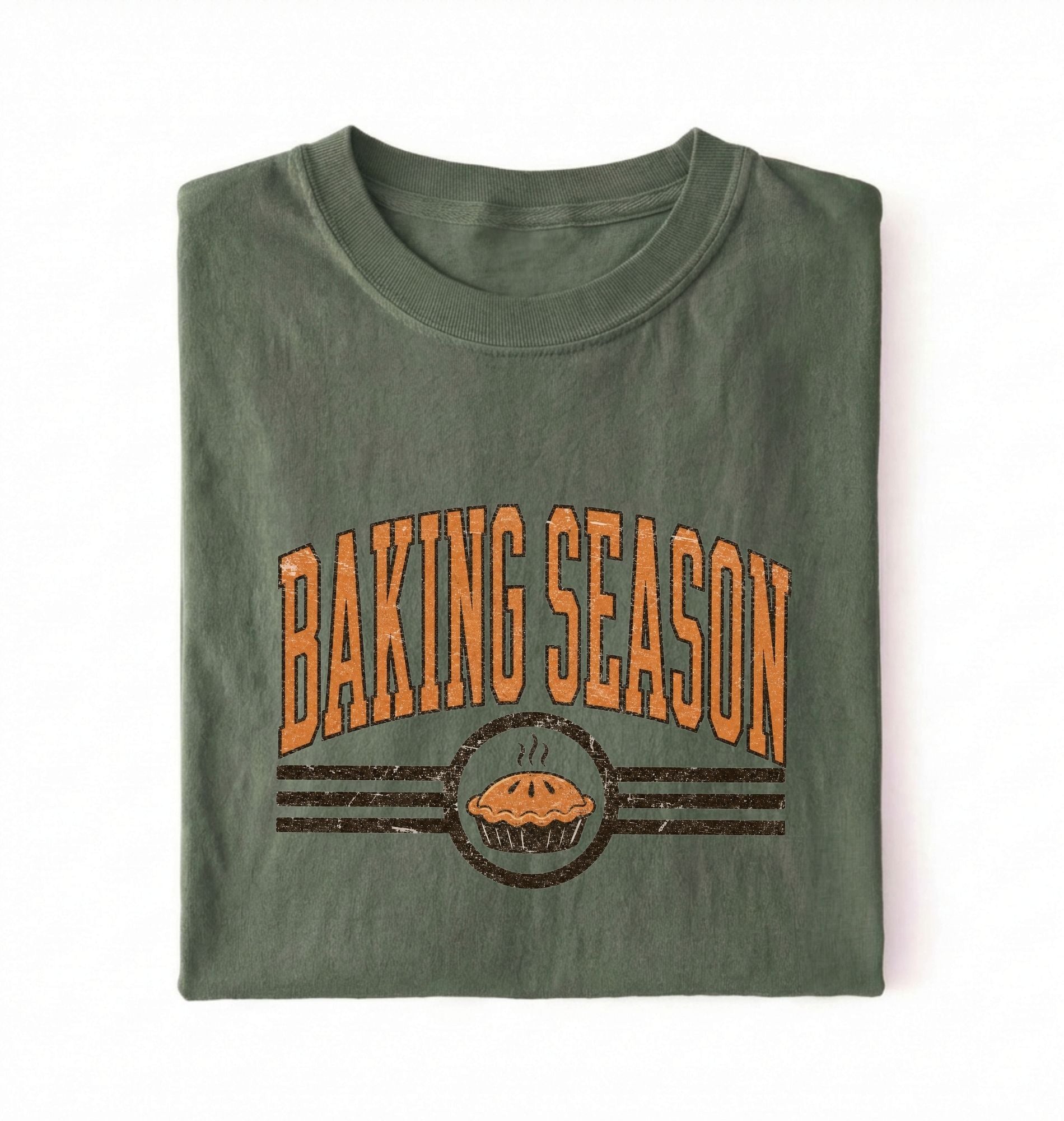A folded olive green t-shirt with a distressed orange and brown graphic that reads 'BAKING SEASON' above an illustration of a pie, set against a plain white background.