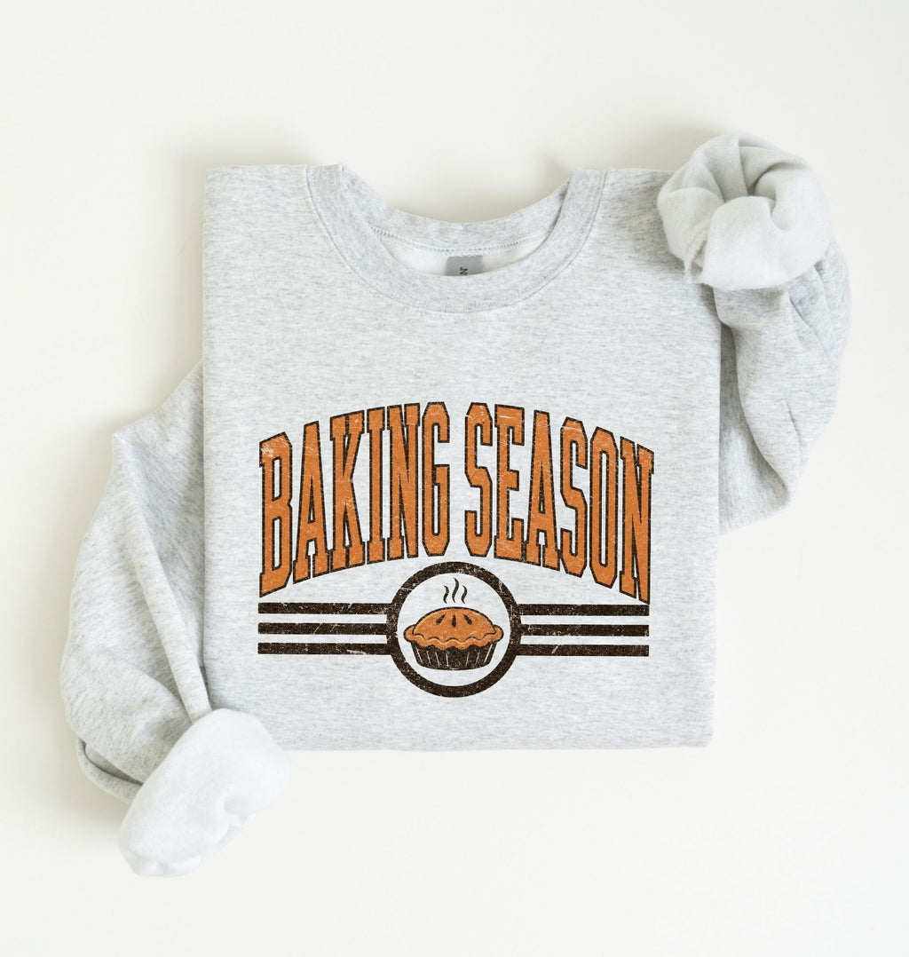 A light heather gray sweatshirt laid flat on a white background, featuring a 'BAKING SEASON' graphic in orange and brown with a pie illustration.