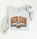 A light heather gray sweatshirt laid flat on a white background, featuring a 'BAKING SEASON' graphic in orange and brown with a pie illustration.