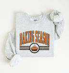 A light heather gray sweatshirt laid flat on a white background, featuring a 'BAKING SEASON' graphic in orange and brown with a pie illustration.