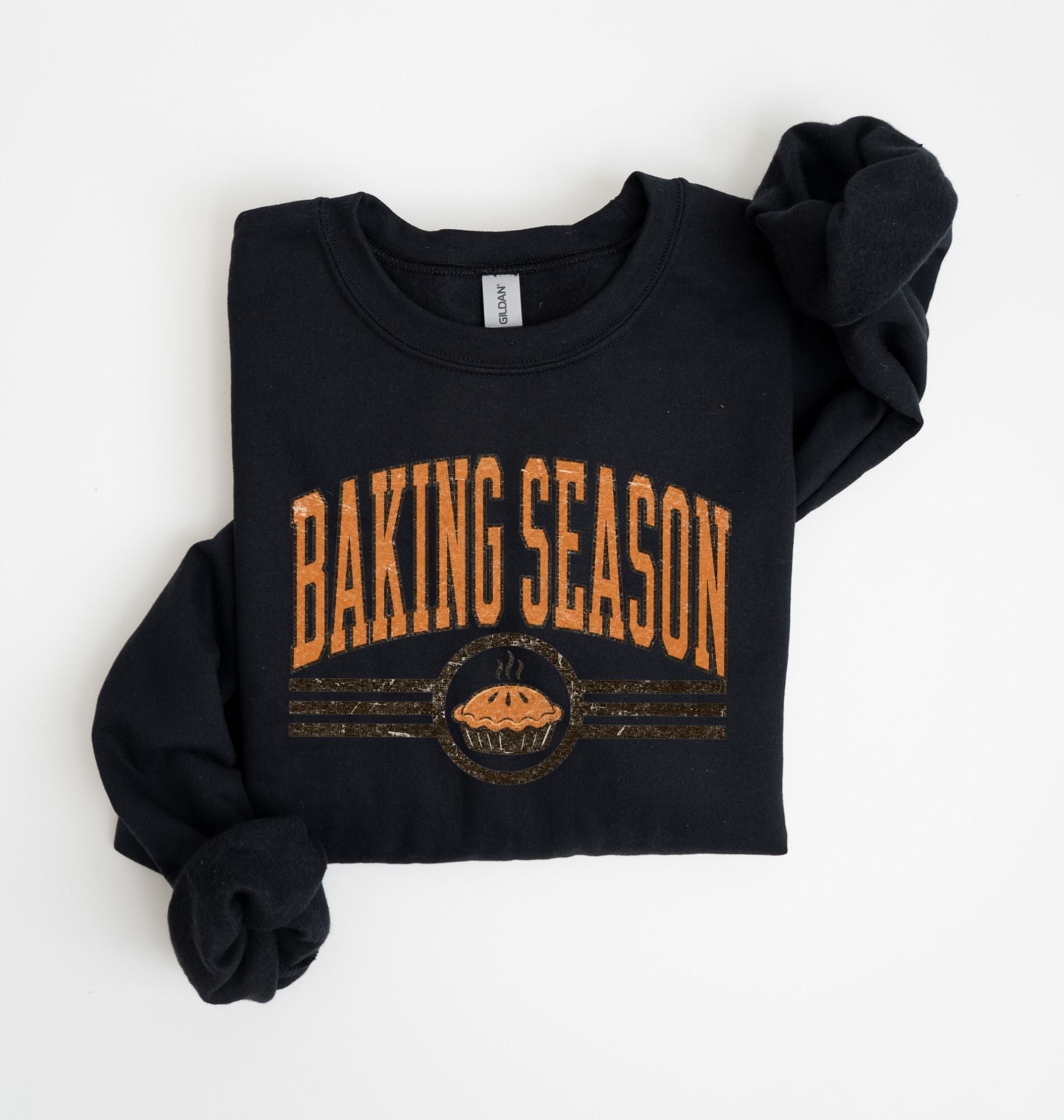 A black long-sleeve sweatshirt with 'BAKING SEASON' printed in distressed orange letters across the chest, featuring a pie graphic below, laid flat on a white background.