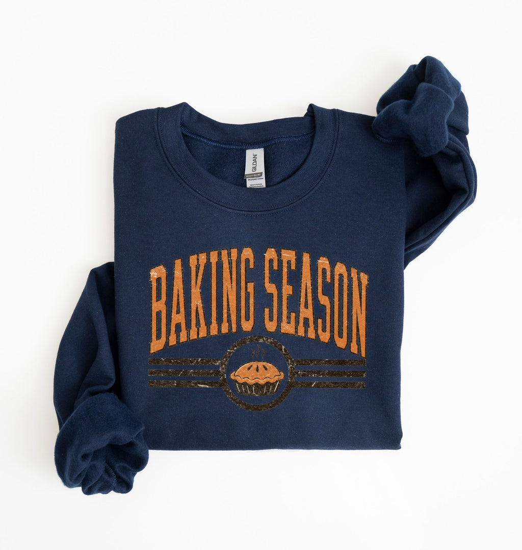 A navy blue long-sleeve sweatshirt with 'BAKING SEASON' printed in orange across the chest, featuring a pie graphic below, laid flat on a white background.