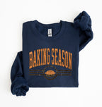 A navy blue long-sleeve sweatshirt with 'BAKING SEASON' printed in orange across the chest, featuring a pie graphic below, laid flat on a white background.