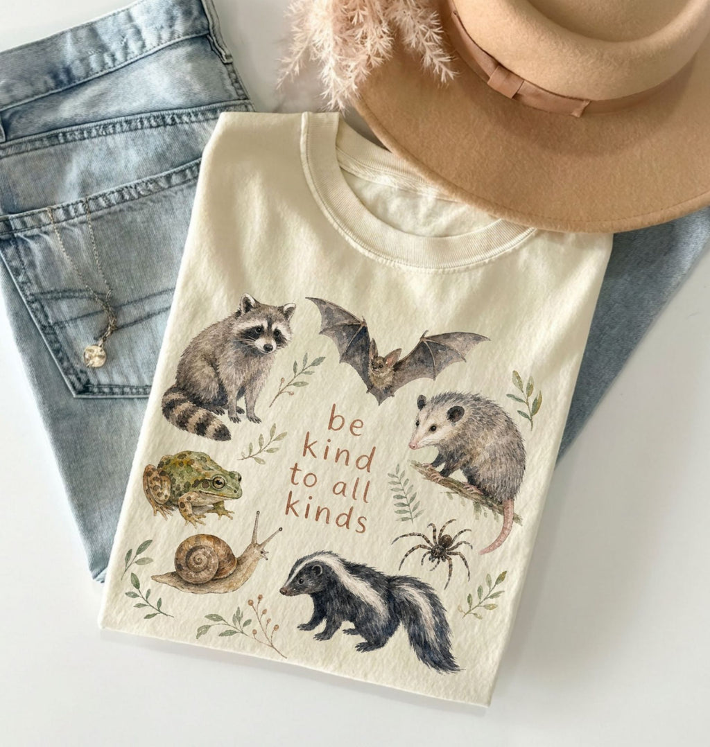 T-shirt with animal illustrations and 'be kind to all kinds' text, displayed with denim jeans and a beige hat.