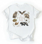 Flat lay of a white Cottagecore Be Kind To All Kinds shirt with woodland animals illustration on a white background