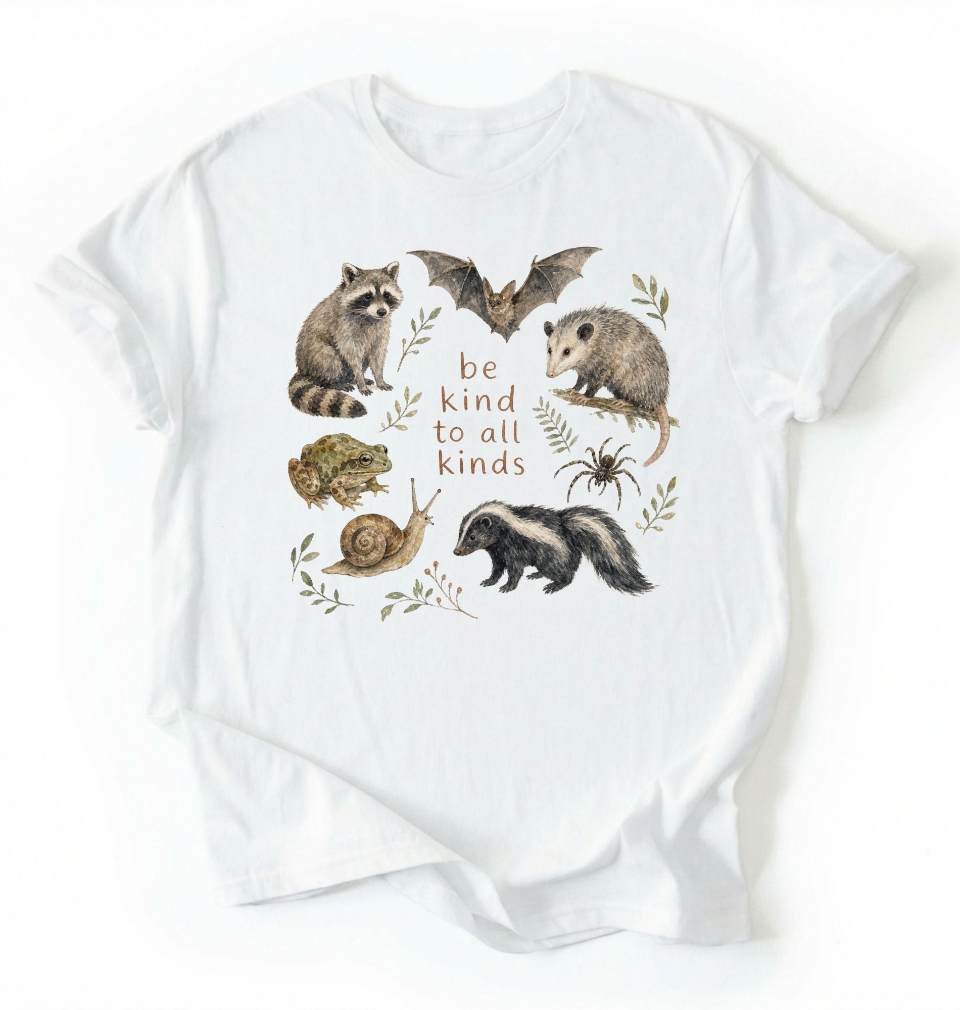 Flat lay of a white Cottagecore Be Kind To All Kinds shirt with woodland animals illustration on a white background