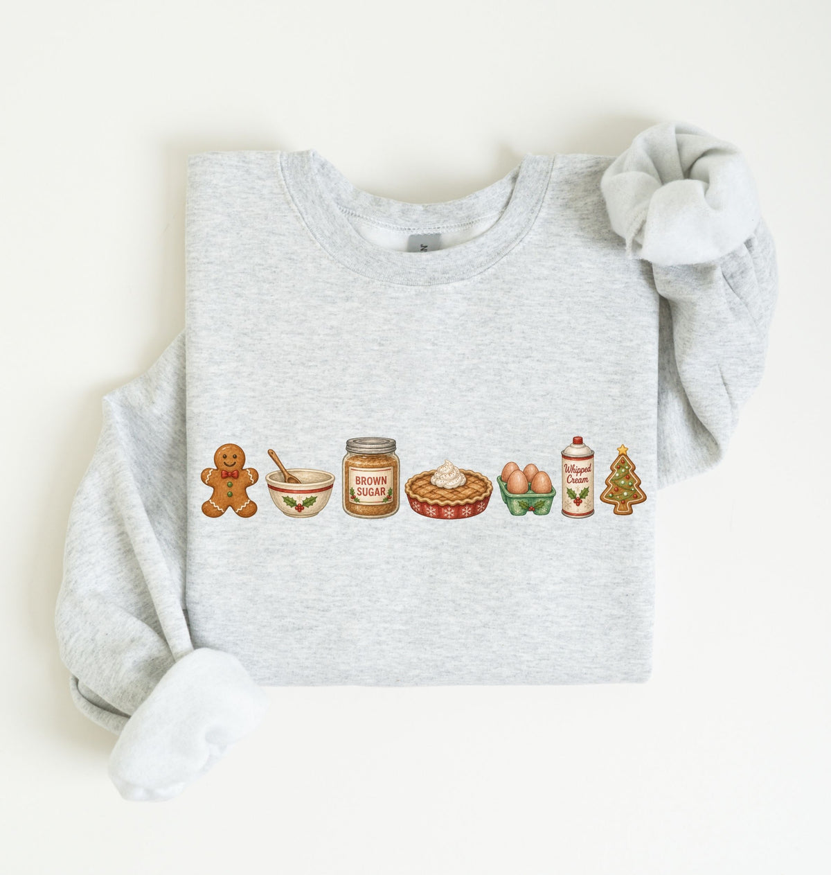A light heather gray long-sleeve sweatshirt with a horizontal row of cute holiday baking illustrations printed on the chest, displayed flat against a warm off-white background.