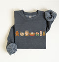 A dark heather gray crewneck sweatshirt with long sleeves, laid flat on a light cream background. The front of the sweatshirt features a horizontal row of colorful Christmas-themed food illustrations, including a gingerbread man, a bowl, a jar of peanut butter, a pie, eggs, hot chocolate, and a Christmas tree.