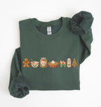 A dark green crewneck sweatshirt with a holiday-themed food line graphic on the chest, styled flat on a white background with a matching green knit scrunchie.