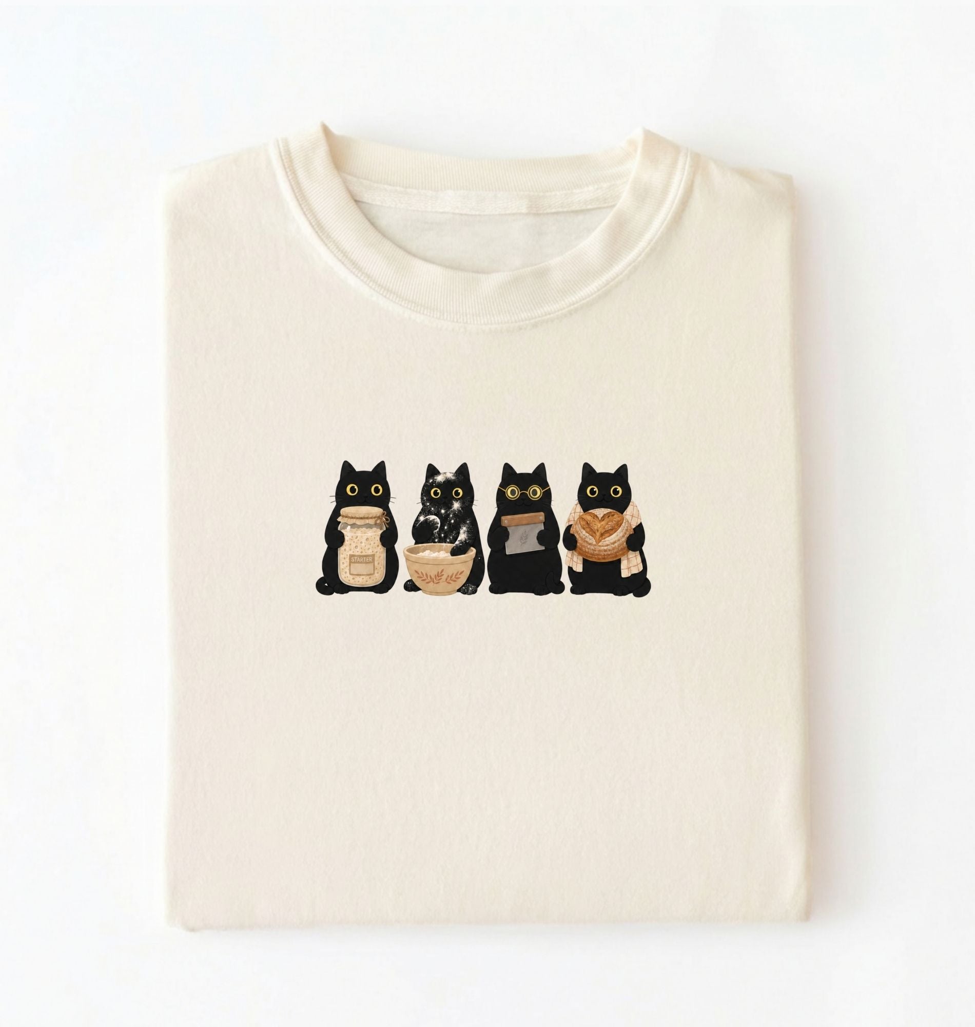 Flat lay of a Cute black cat baker shirt featuring baking cats with bread and mixing bowl on cream t-shirt on a white background 