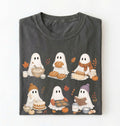 A dark charcoal gray t-shirt folded neatly, featuring a cute graphic print of six white ghosts baking autumn treats like bread, cakes, and cookies, surrounded by pumpkins, fall leaves, and cozy scarves.