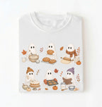 A white short-sleeve crewneck t-shirt with a cute cartoon graphic of six ghosts baking autumn treats, displayed on a clean white background.
