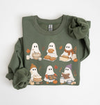 An olive green crewneck sweatshirt featuring a cute cartoon graphic of six ghosts dressed in autumn outfits (hat, scarf, boots, and masks) while eating fall foods like bread, pumpkin pie, and cookies. The sweatshirt is styled flat on a white background with rolled-up sleeves and a matching fabric scrunchie.
