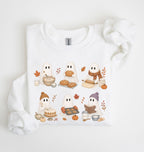A white long-sleeve crewneck sweatshirt featuring a cute cartoon graphic of six ghosts baking and eating autumn treats, styled on a white background with a matching fabric scrunchie.