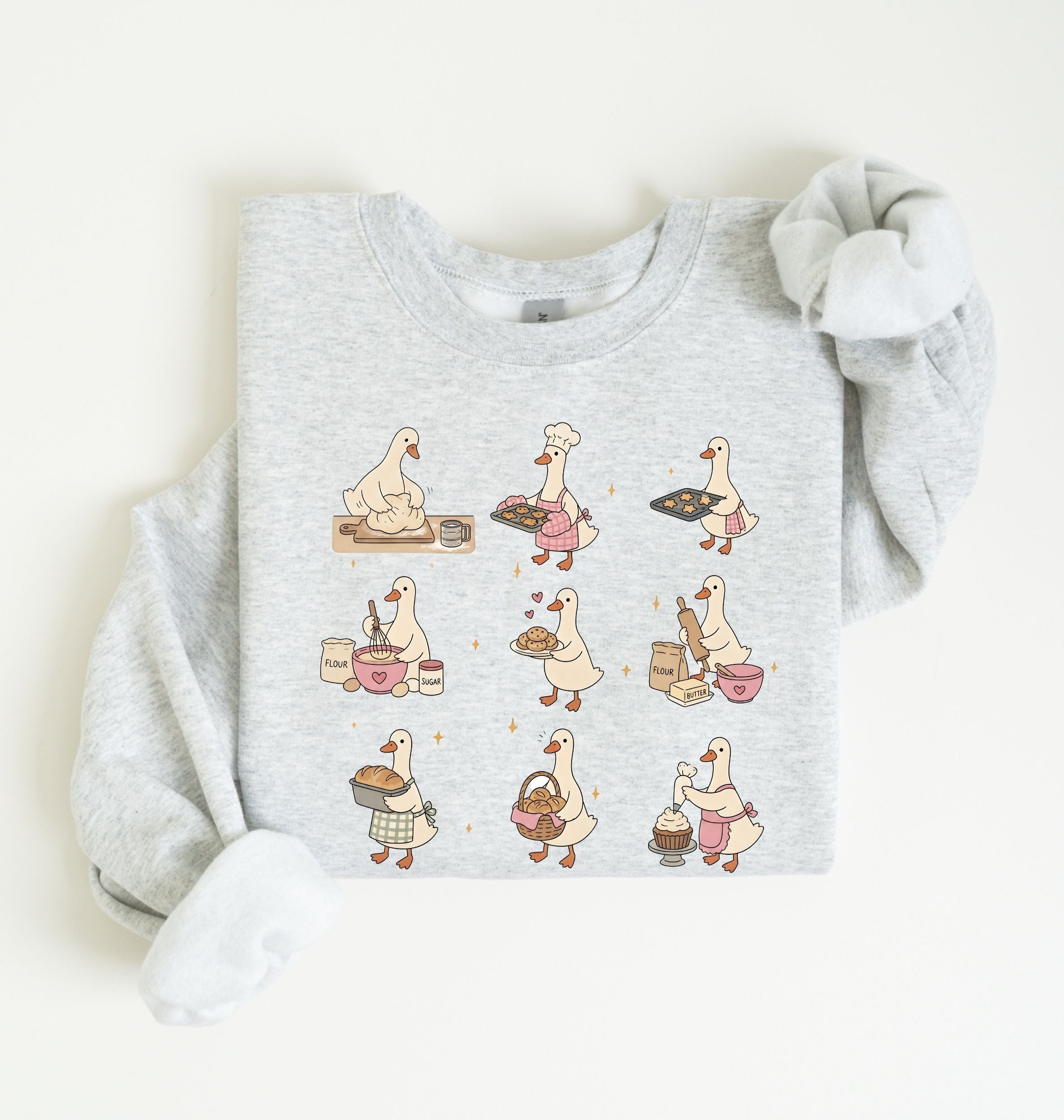 A light heather gray long-sleeve sweatshirt with a graphic print of nine cartoon geese in various baking poses, styled flat on a light white background.