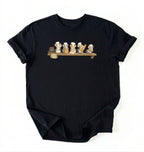 A black short-sleeve crewneck t-shirt featuring a graphic print of five cartoon cats wearing white chef hats lined up on a wooden shelf, displayed against a plain white background.