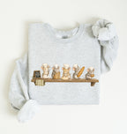A light heather gray long-sleeve sweatshirt with a graphic of five cute cartoon mice dressed as chefs sitting on a wooden shelf, displayed flat on a warm off-white background.