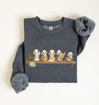 A folded dark heather gray sweatshirt featuring a cute graphic of five cartoon mice dressed as chefs sitting on a wooden shelf. The sleeves are rolled up, and the sweatshirt is photographed flat against a clean, off-white background.