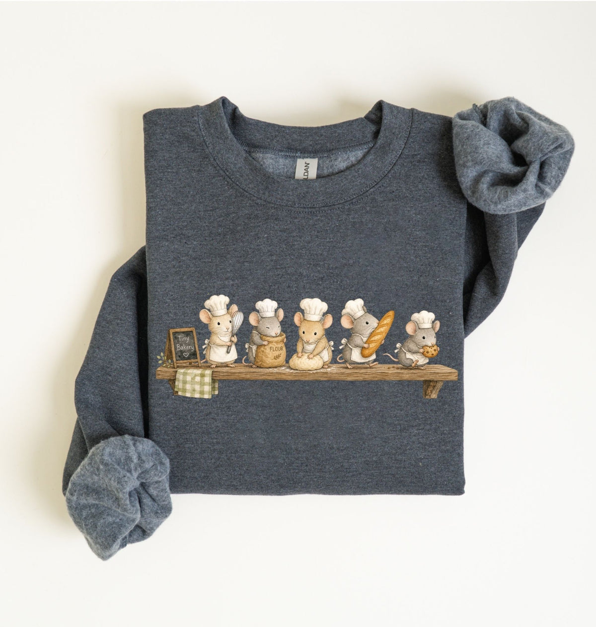 A folded dark heather gray sweatshirt featuring a cute graphic of five cartoon mice dressed as chefs sitting on a wooden shelf. The sleeves are rolled up, and the sweatshirt is photographed flat against a clean, off-white background.