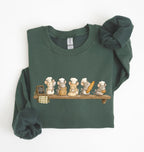A dark green long-sleeve sweatshirt with a graphic of six cartoon mice dressed as chefs sitting on a wooden shelf. The sweatshirt is neatly folded with the sleeves rolled up, set against a plain white background.
