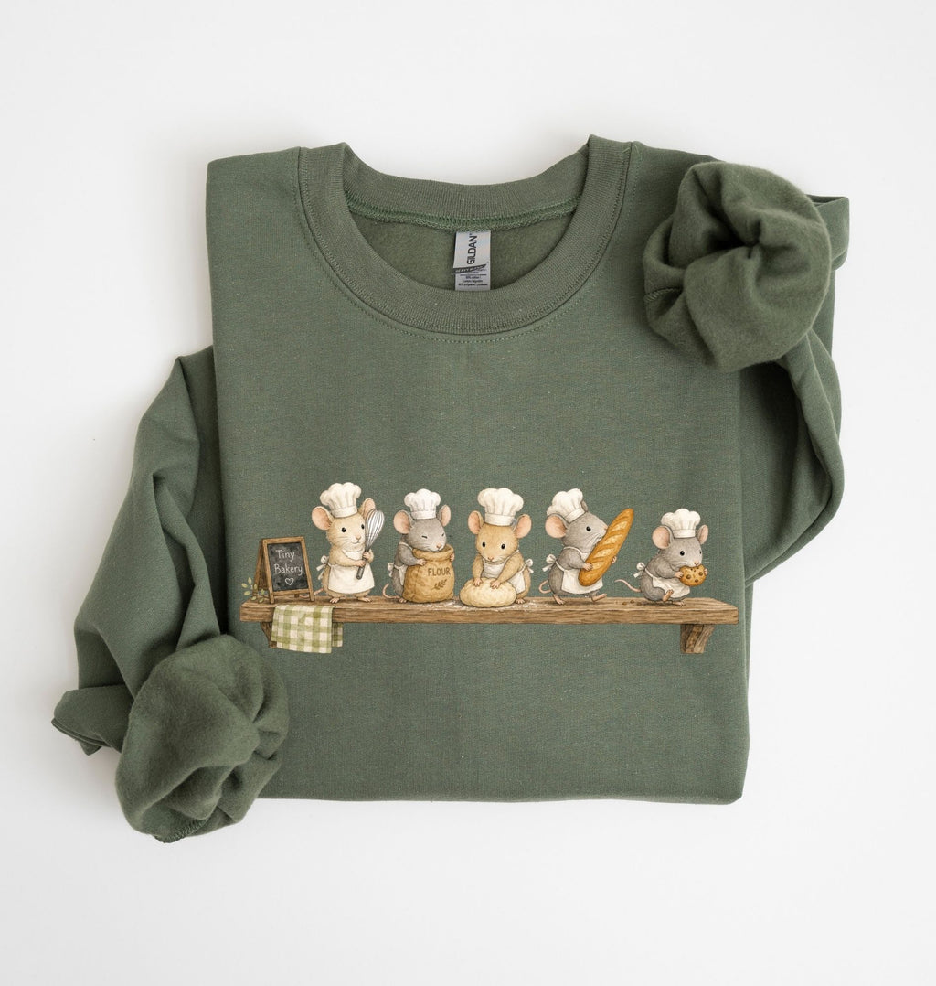 An olive green long-sleeve sweatshirt with a graphic of five cartoon mice wearing chef hats and holding baking utensils on a wooden shelf, displayed flat on a white background.