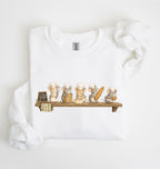 A white long-sleeve sweatshirt laid flat on a white background, featuring a printed graphic of five cute cartoon mice dressed as chefs sitting on a wooden shelf with bread and baking items.