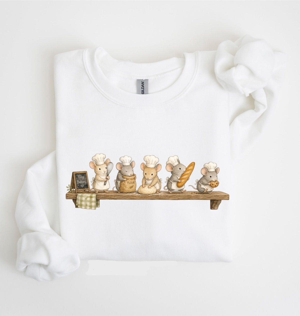 A white long-sleeve sweatshirt laid flat on a white background, featuring a printed graphic of five cute cartoon mice dressed as chefs sitting on a wooden shelf with bread and baking items.