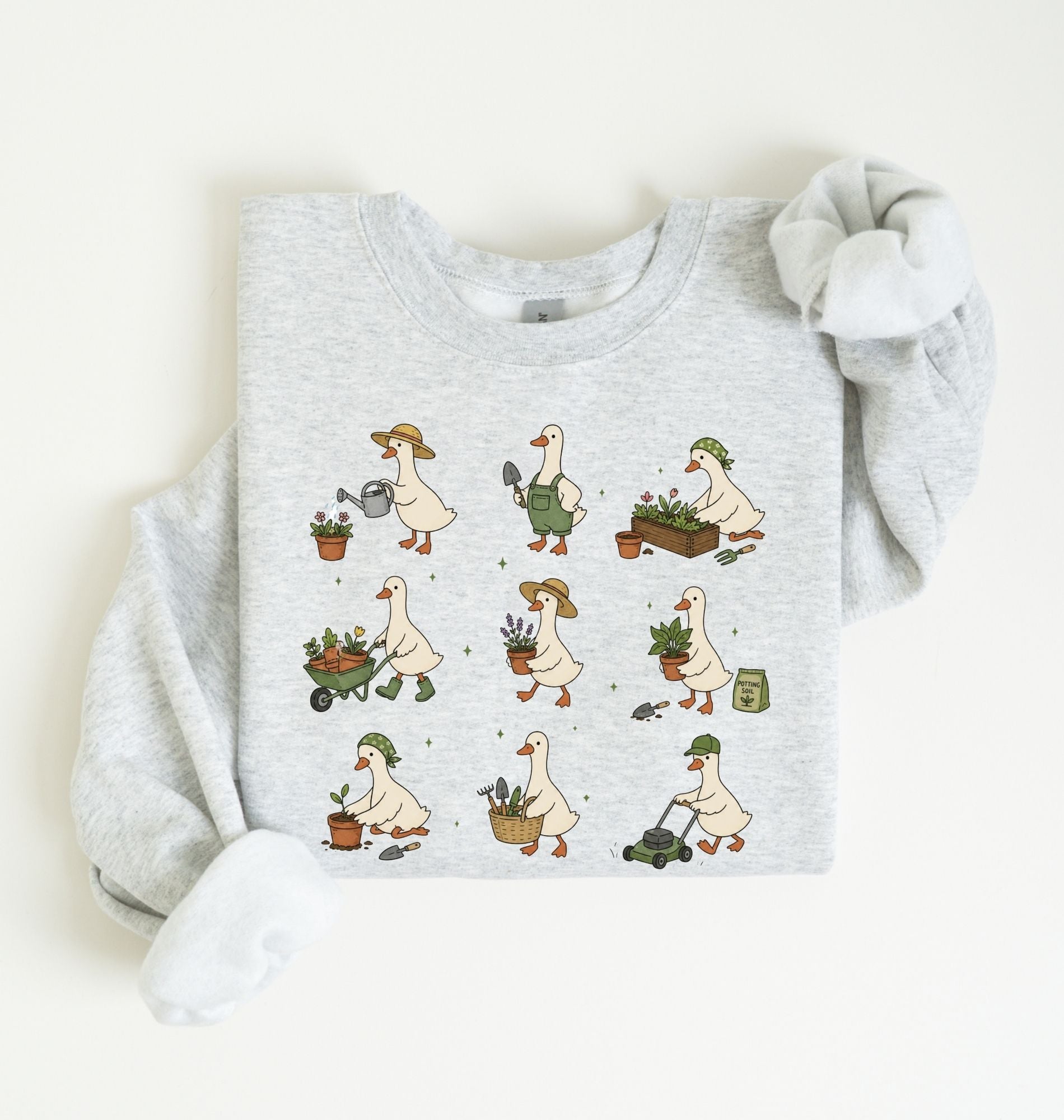 A light heather gray sweatshirt with a long-sleeve cuff rolled up, featuring a graphic print of a cartoon goose showing different gardening activities in a nine-step sequence on a white background 