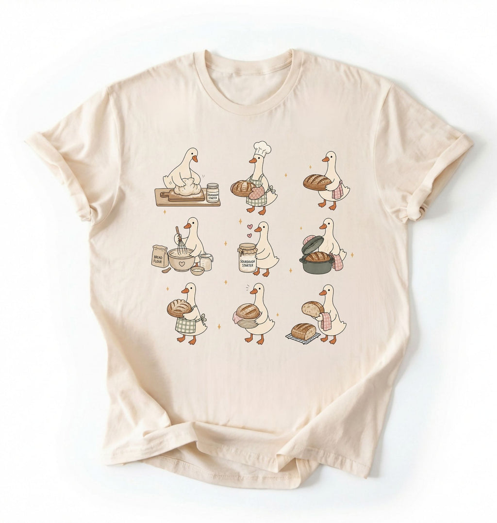 Flat lay of a Cute goose baker shirt with sourdough bread and cottagecore baking artwork on cream tee on a white background 