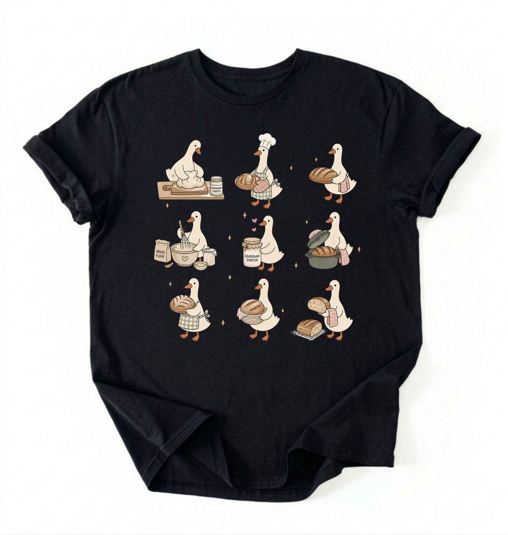 Flat lay of a Cute goose baker shirt with sourdough bread and cottagecore baking artwork on black tee on a white background 