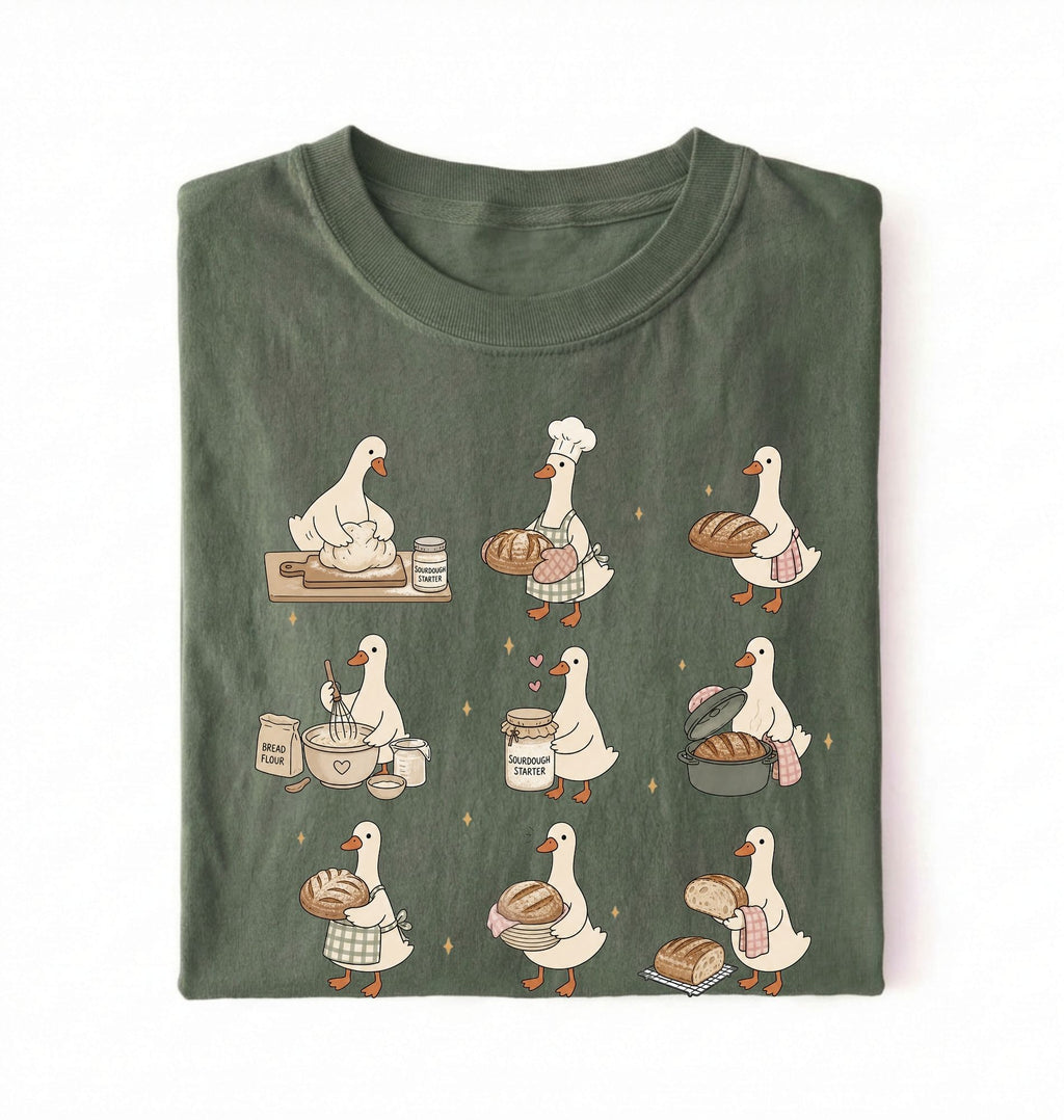 Flat lay of a Cute goose baker shirt with sourdough bread and cottagecore baking artwork on green tee on a white background 