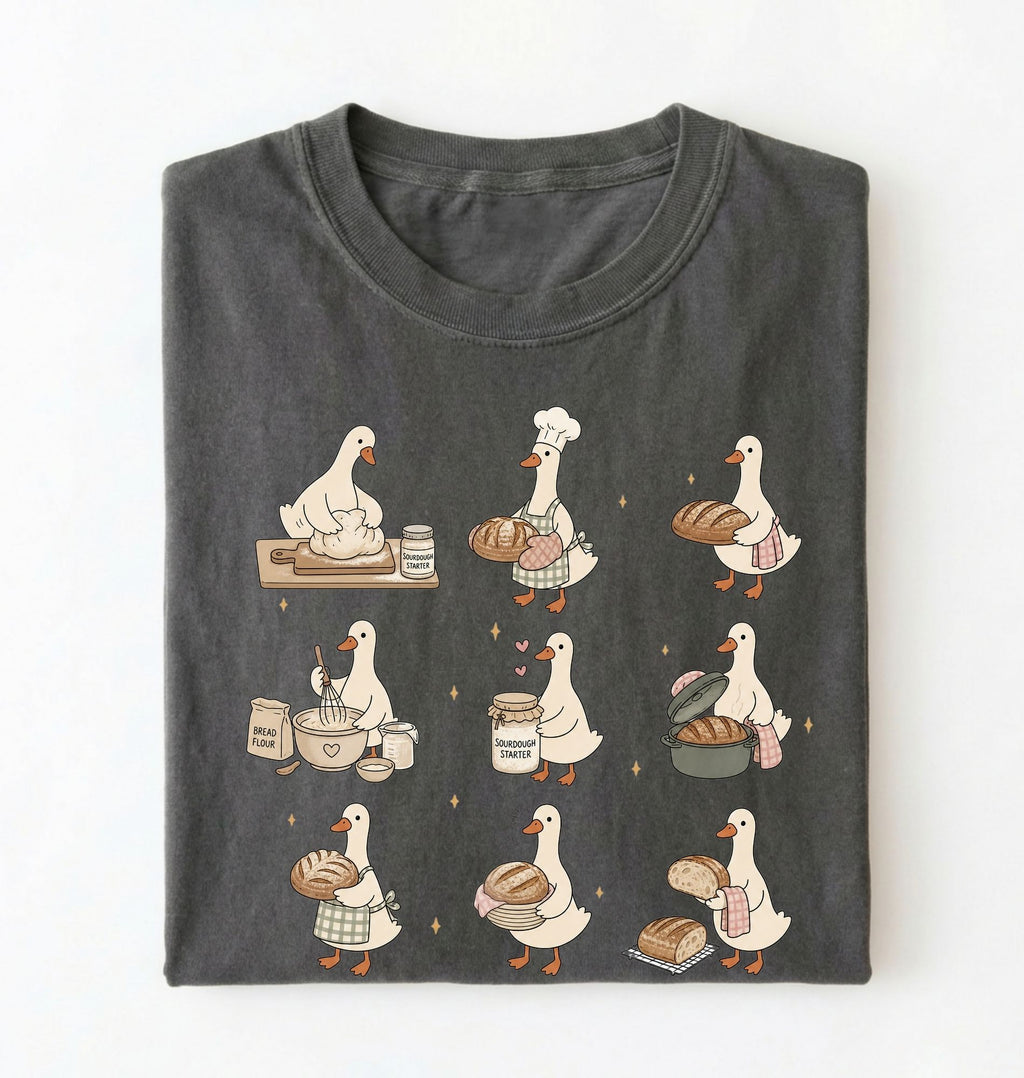 Flat lay of a Cute goose baker shirt with sourdough bread and cottagecore baking artwork on pepper tee on a white background 