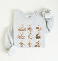 A light heather gray long-sleeve sweatshirt with a graphic print of nine cartoon geese in various baking and bread-related poses, styled flat on a light cream background.