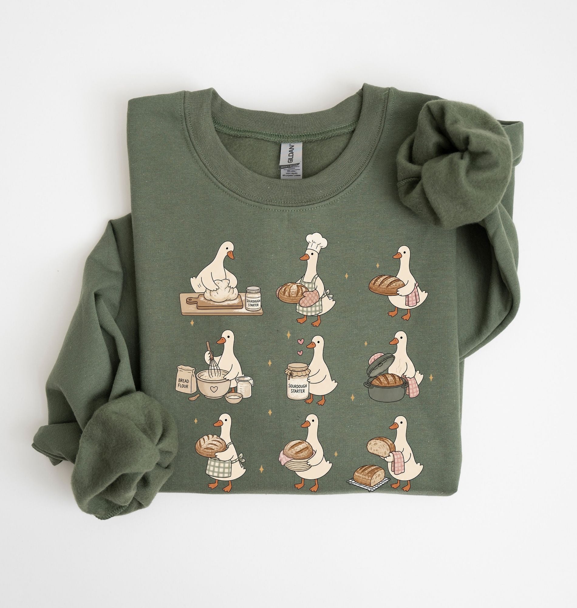 An olive green long-sleeve sweatshirt with a graphic print of nine bakers' ducks in various cooking and baking poses, shown folded on a white background.