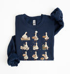 A navy blue long-sleeve sweatshirt with a graphic print of nine cartoon ducks in various cooking and baking poses, shown folded on a white background.