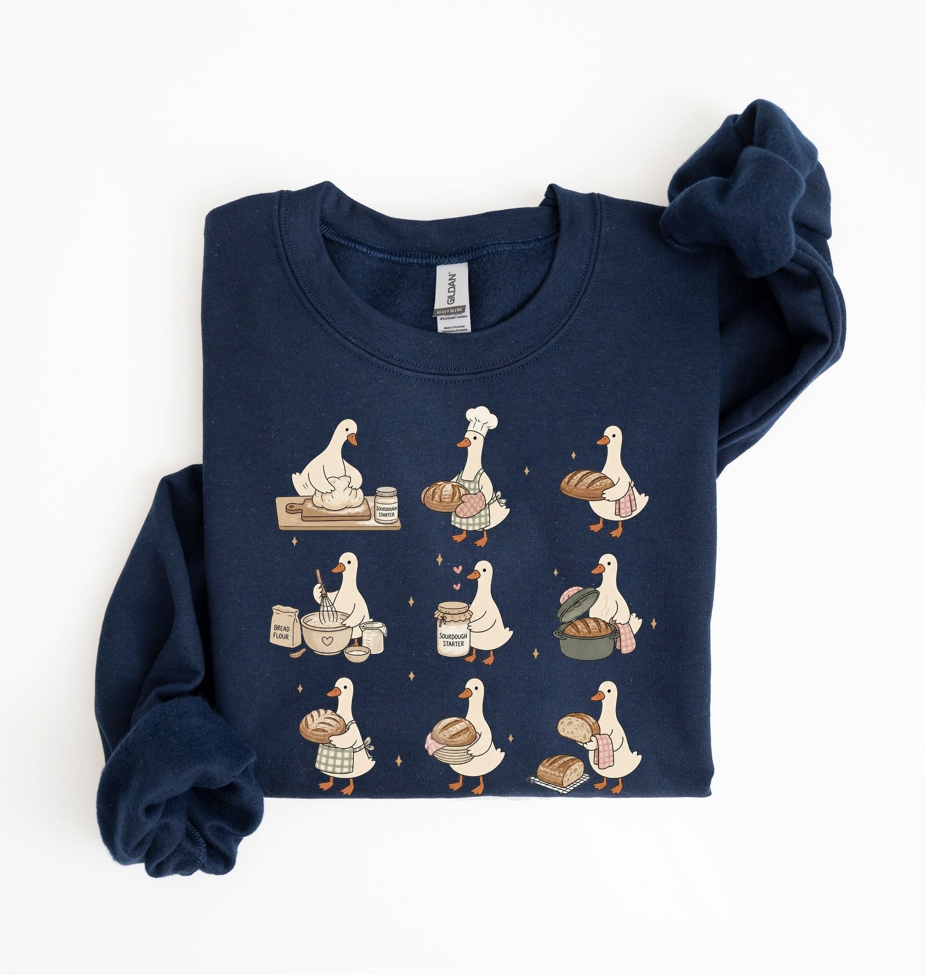 A navy blue long-sleeve sweatshirt with a graphic print of nine cartoon ducks in various cooking and baking poses, shown folded on a white background.