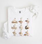 A white crewneck sweatshirt with a graphic print of nine cartoon ducks dressed as bakers, shown folded on a white background with a matching white ribbon.