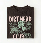 Flat lay of an espresso t-shirt featuring plant illustrations and bold text reading “Dirt Nerd Club.” on a white background
