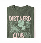 Flat lay of a moss t-shirt featuring plant illustrations and bold text reading “Dirt Nerd Club.” on a white background