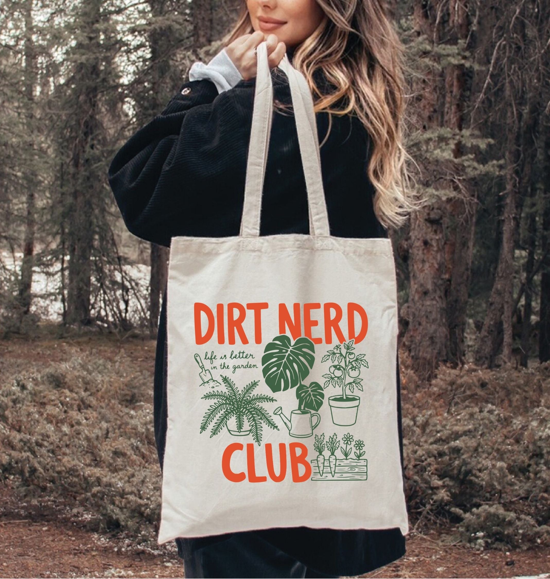 Person holding a tote bag with 'Dirt Nerd Club' text and plant illustrations in a forest setting