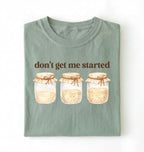 Flat lay of a bay t-shirt featuring illustrated jars and text reading “Don’t Get Me Started. Funny sourdough starter perfect gift for bakers fermentation lovers and bread enthusiasts on a white background