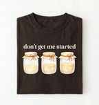 Flat lay of a dark chocolate t-shirt featuring illustrated jars and text reading “Don’t Get Me Started. Funny sourdough starter perfect gift for bakers fermentation lovers and bread enthusiasts on a white background