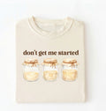 Flat lay of a ivory t-shirt featuring illustrated jars and text reading “Don’t Get Me Started. Funny sourdough starter perfect gift for bakers fermentation lovers and bread enthusiasts on a white background