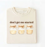 Flat lay of a ivory t-shirt featuring illustrated jars and text reading “Don’t Get Me Started. Funny sourdough starter perfect gift for bakers fermentation lovers and bread enthusiasts on a white background