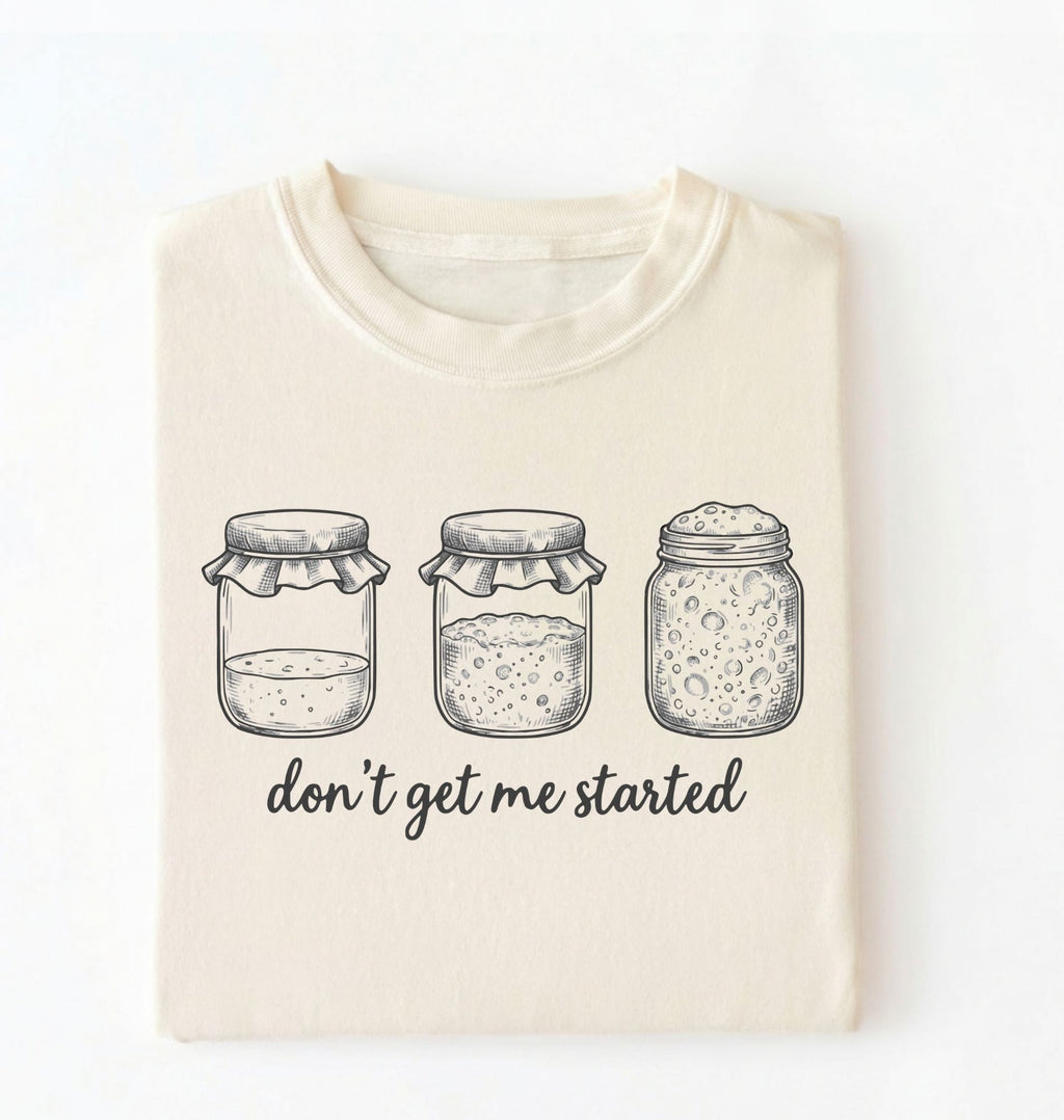 Flat lay of an ivory Funny sourdough shirt with starter jars illustration perfect gift for bakers and fermentation lovers on a white background
