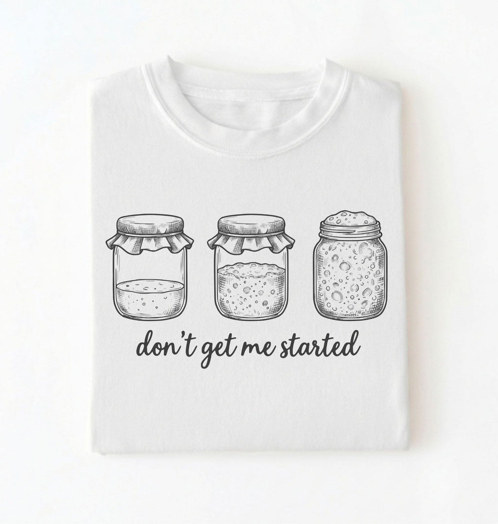 Flat lay of a white Funny sourdough shirt with starter jars illustration perfect gift for bakers and fermentation lovers on a white background
