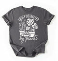 A Charcoal color shirt with a text written "easily distracted by plants" with houseplant illustration plant lover gift on a white background 