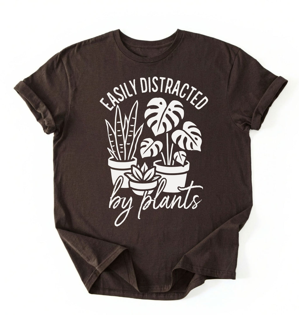A dark_chocolate color shirt with a text written "easily distracted by plants" with houseplant illustration plant lover gift on a white background 