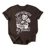 A dark_chocolate color shirt with a text written "easily distracted by plants" with houseplant illustration plant lover gift on a white background 