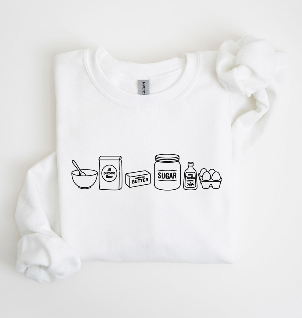 A white long-sleeve sweatshirt laid flat on a white background, featuring a black line art graphic of baking ingredients: a bowl, flour bag, butter stick, sugar jar, vanilla bottle, and eggs.